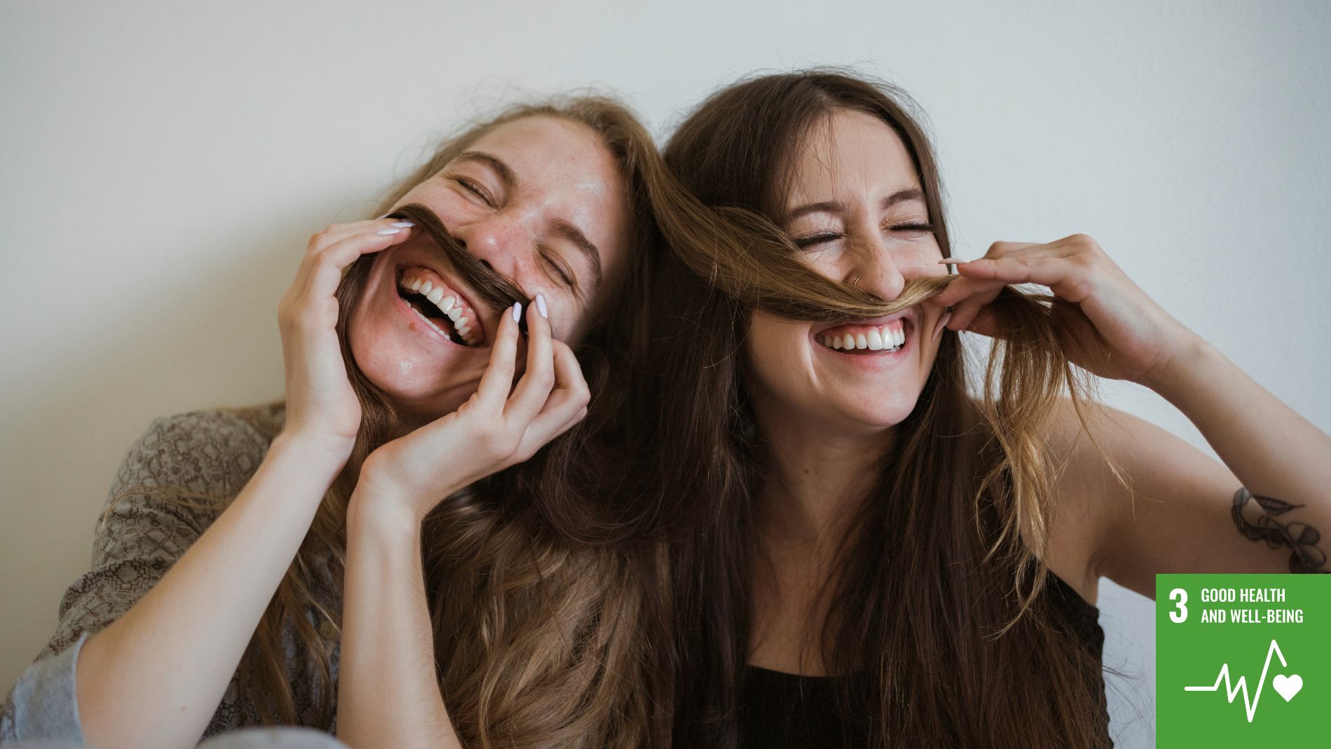 Two smiling women use their hair to create a mustache.
